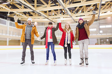 Image showing happy friends waving hands on skating rink