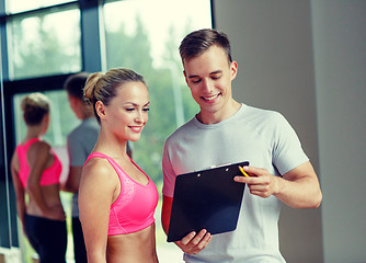 Image showing smiling young woman with personal trainer in gym