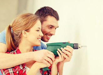 Image showing smiling couple drilling hole in wall at home