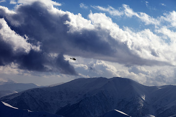 Image showing Helicopter in cloudy sky and winter mountains in evening