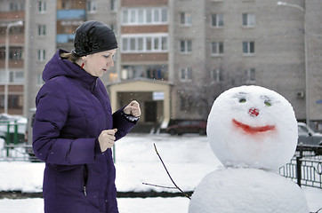 Image showing The woman near a snowman in the yard of the house.