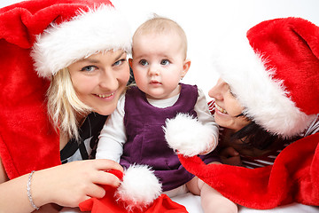 Image showing smiling infant baby with two womans with santa hats