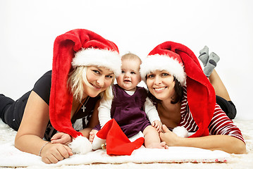 Image showing smiling infant baby with two womans with santa hats