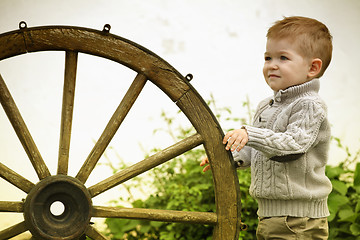 Image showing 2 years old curious Baby boy with old wooden wheel 