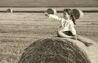 Image showing small rural girl on the straw after harvest field with straw bal