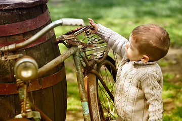 Image showing 2 years old curious Baby boy walking around the old bike 