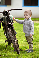 Image showing 2 years old curious Baby boy walking around the old bike 