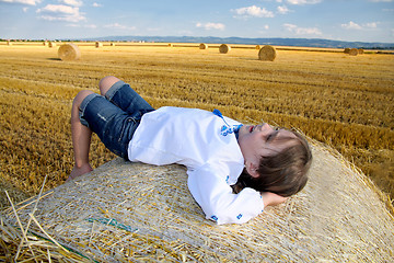 Image showing small rural girl on the straw after harvest field with straw bal