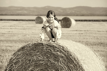 Image showing small rural girl on the straw after harvest field with straw bal