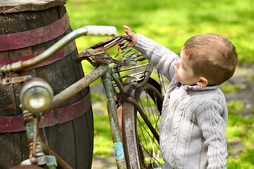 Image showing 2 years old curious boy walking around the old bike 