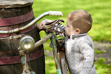 Image showing 2 years old curious Baby boy walking around the old bike 