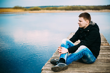 Image showing Young handsome man sitting on wooden pier, relaxing,  thinking, 