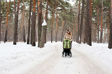 Image showing Young mother with baby carriage in winter forest