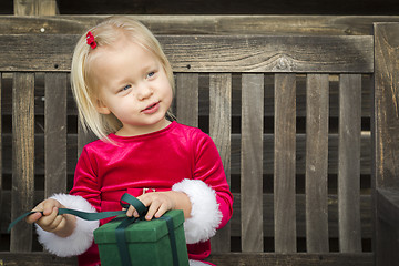 Image showing Adorable Little Girl Unwrapping Her Gift on a Bench