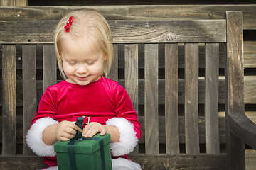 Image showing Adorable Little Girl Unwrapping Her Gift on a Bench