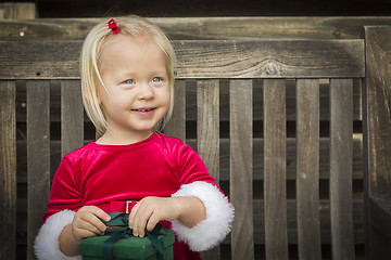 Image showing Adorable Little Girl Unwrapping Her Gift on a Bench