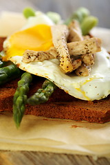 Image showing Toast with egg, green asparagus and turkey on the old board..