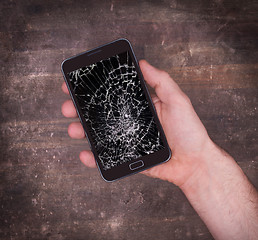 Image showing Hand holding a mobile phone with a broken screen