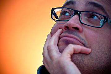 Image showing Bearded caucasian man wearing eyeglasses looking up on orange gr