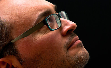 Image showing bearded caucasian man wearing glasses looking up on black