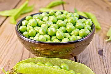 Image showing Green peas in brown bowl and pod on board