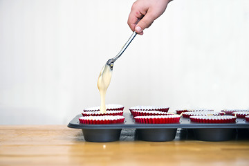 Image showing Filling cupcakes with batter