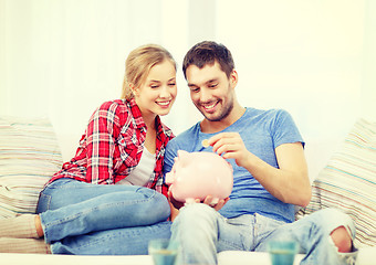 Image showing smiling couple with piggybank sitting on sofa