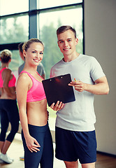 Image showing smiling young woman with personal trainer in gym