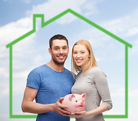 Image showing smiling couple holding piggy bank over green house