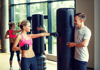 Image showing smiling woman with personal trainer boxing in gym