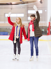 Image showing happy girls friends waving hands on skating rink