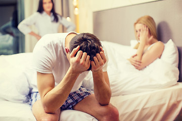 Image showing man sitting on the bed with two women on the back