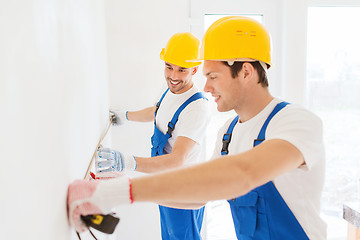 Image showing smiling builders with measuring tape indoors