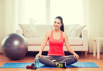 Image showing smiling girl sitting on mat with sports equipment