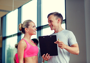 Image showing smiling young woman with personal trainer in gym