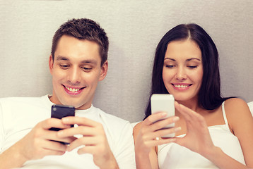 Image showing smiling couple in bed with smartphones