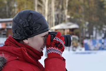 Image showing The woman in winter clothes photographs the SLR camera.