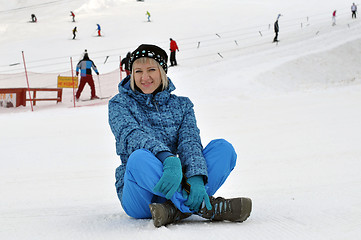 Image showing The woman in winter clothes sits on snow against the ski slope a