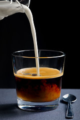 Image showing Pouring milk into a glass of black coffee