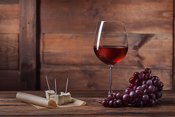 Image showing Red wine in glass with grape and cheese on wood