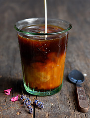 Image showing Pouring milk into a glass of black coffee