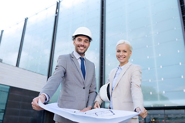 Image showing smiling businessmen with blueprint and helmets