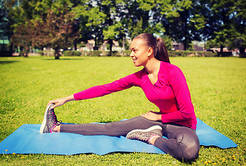 Image showing smiling woman stretching leg on mat outdoors