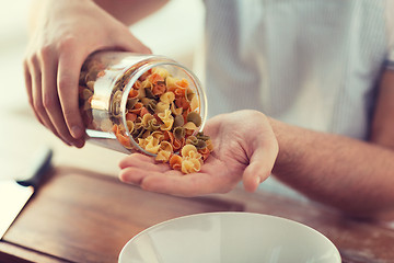 Image showing close up of male emptying jar with colorful pasta