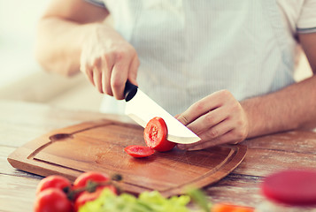 Image showing male hand cutting tomato on board with knife