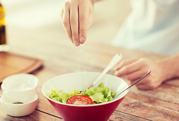 Image showing close up of male hands flavouring salad in a bowl