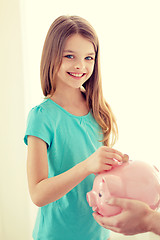 Image showing smiling little girl putting coin into piggy bank