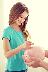 Image showing smiling little girl putting coin into piggy bank