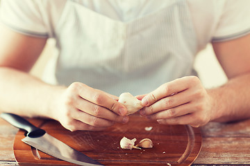 Image showing male hands taking off peel of garlic on board