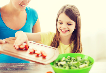 Image showing little girl with mother adding tomatoes to salad